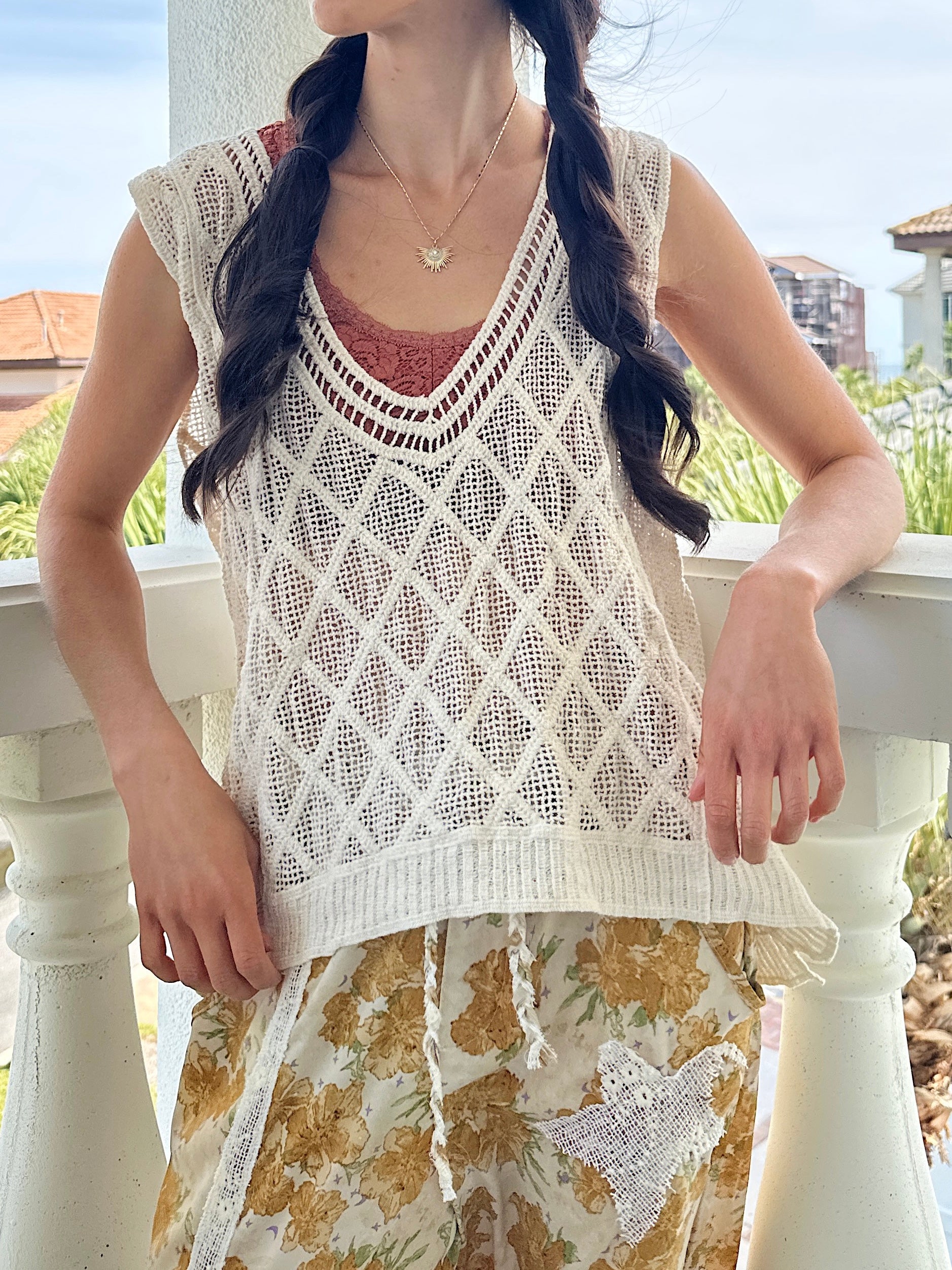 Woman wearing a white crochet top and floral pants on a balcony