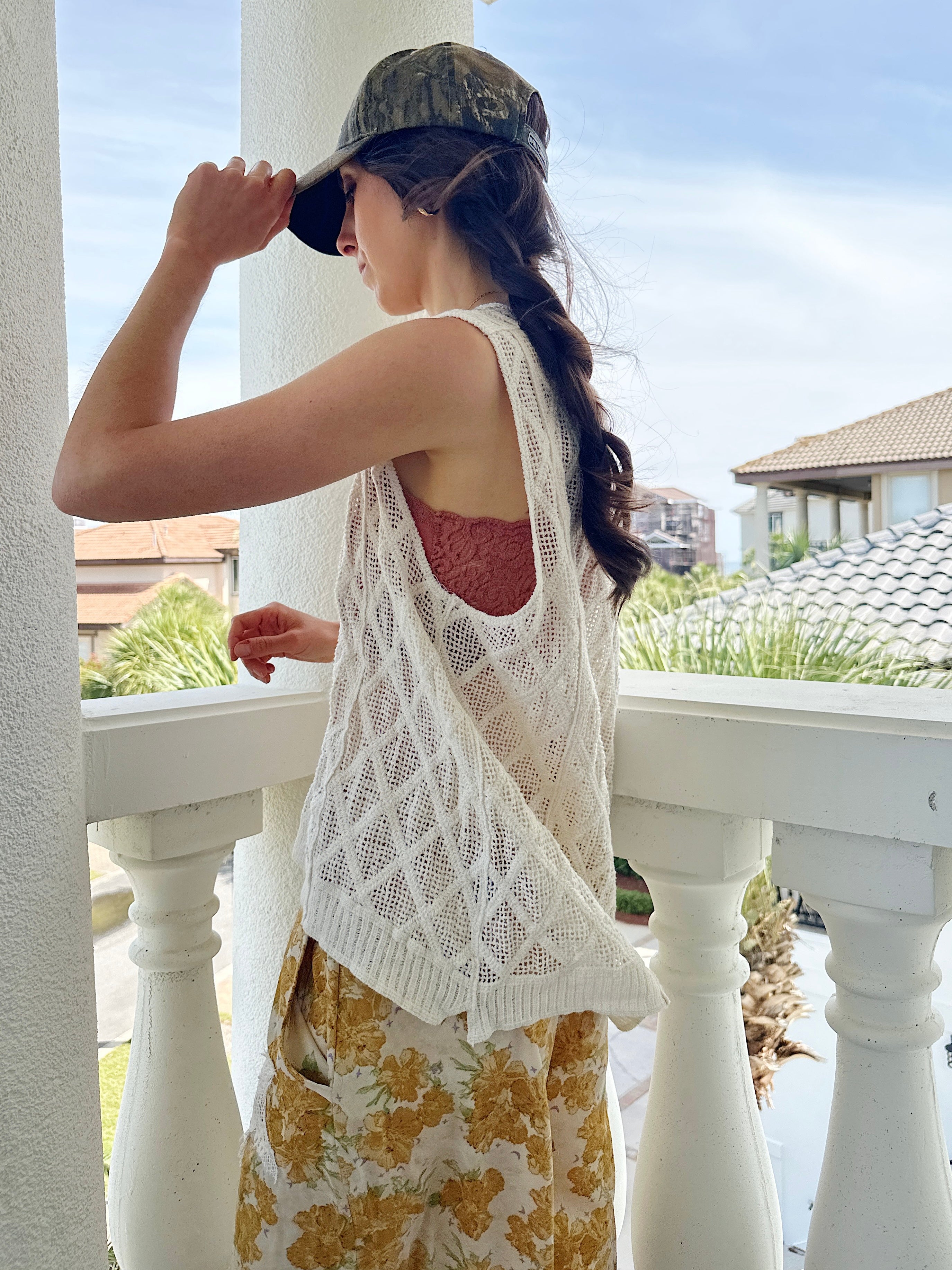 Woman on a balcony wearing a white lace top and yellow floral pants.