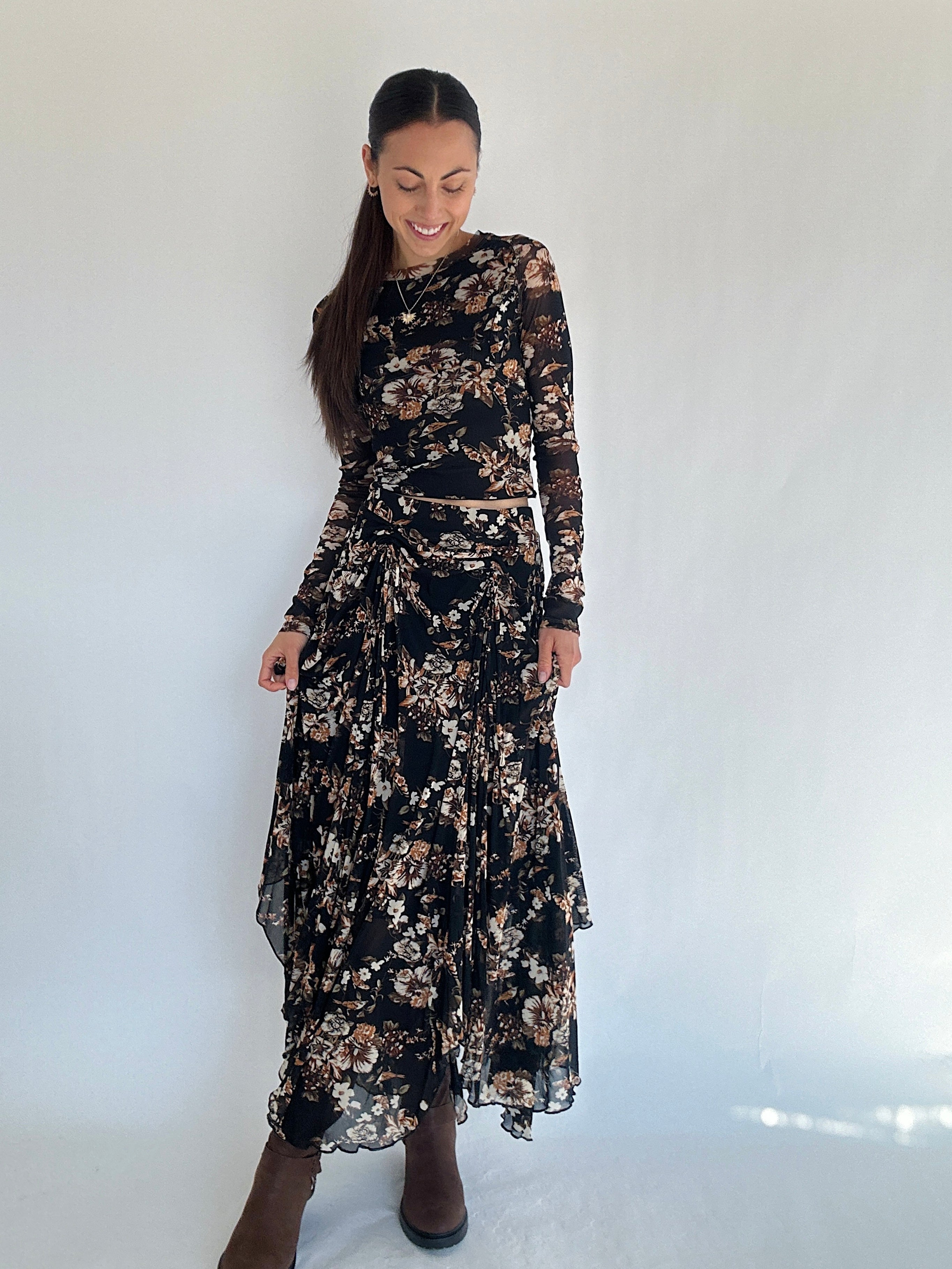 Woman wearing a black floral mesh maxi skirt and matching long sleeve top against a white background