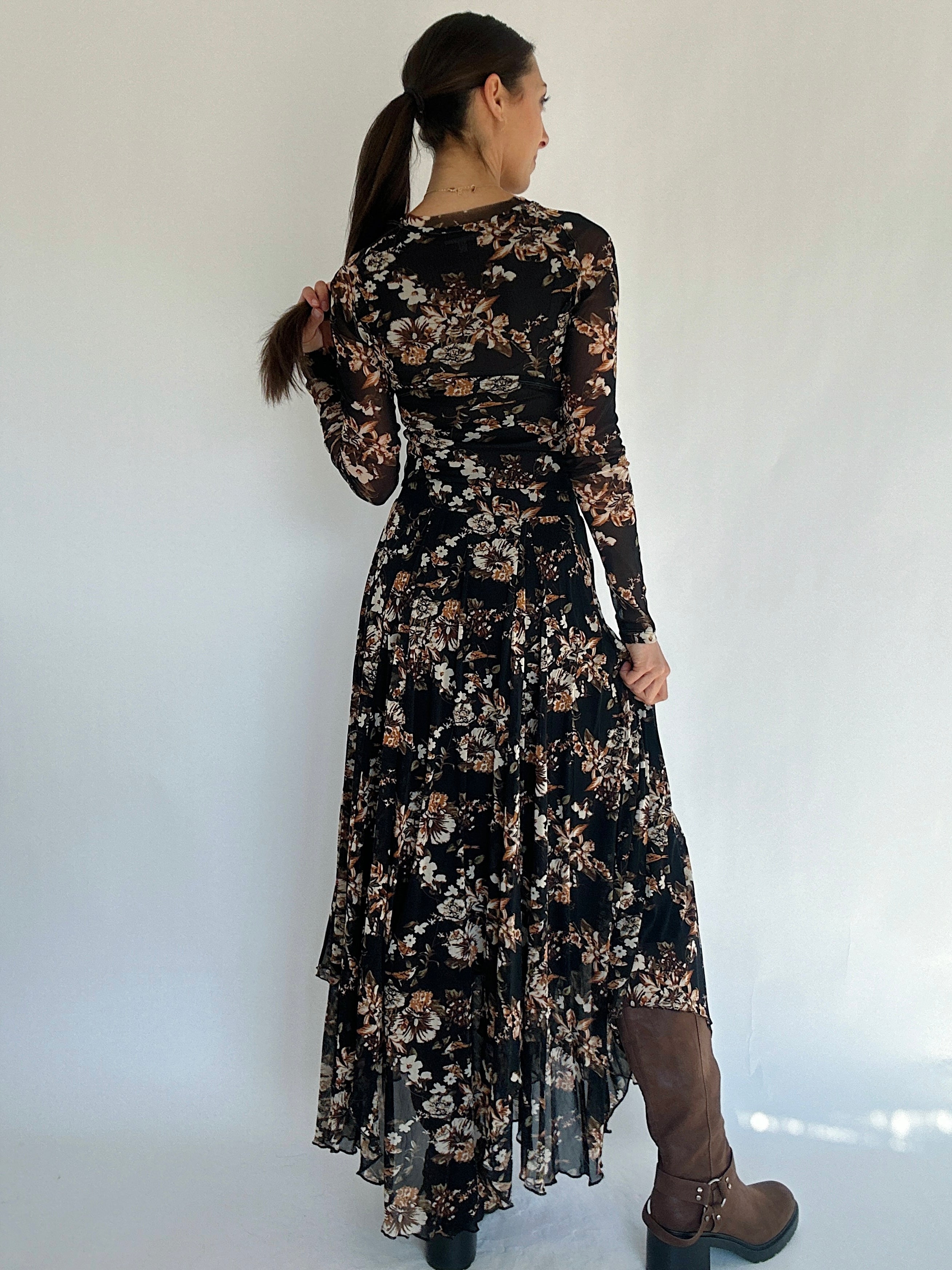 Woman wearing a black floral maxi skirt and matching top against a white background back view