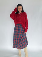 Woman wearing a red cardigan and red and blue plaid skirt on a white background