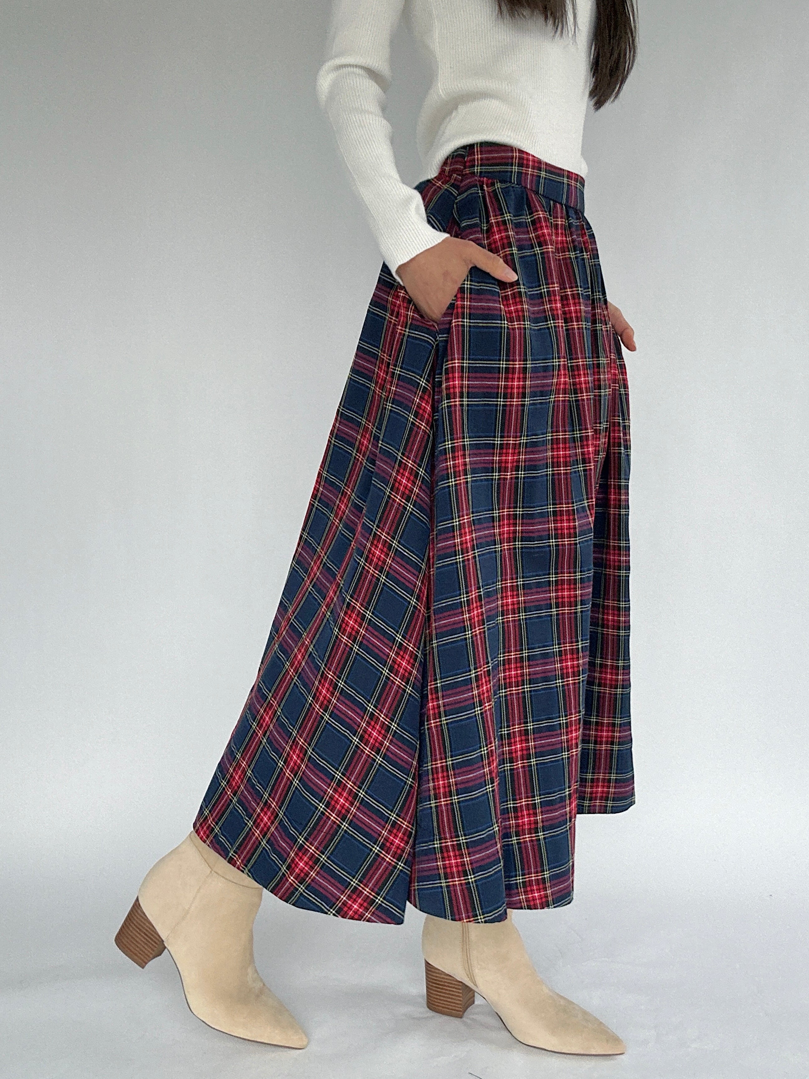 Person wearing a red and navy plaid skirt with hands in side pockets on a plain background