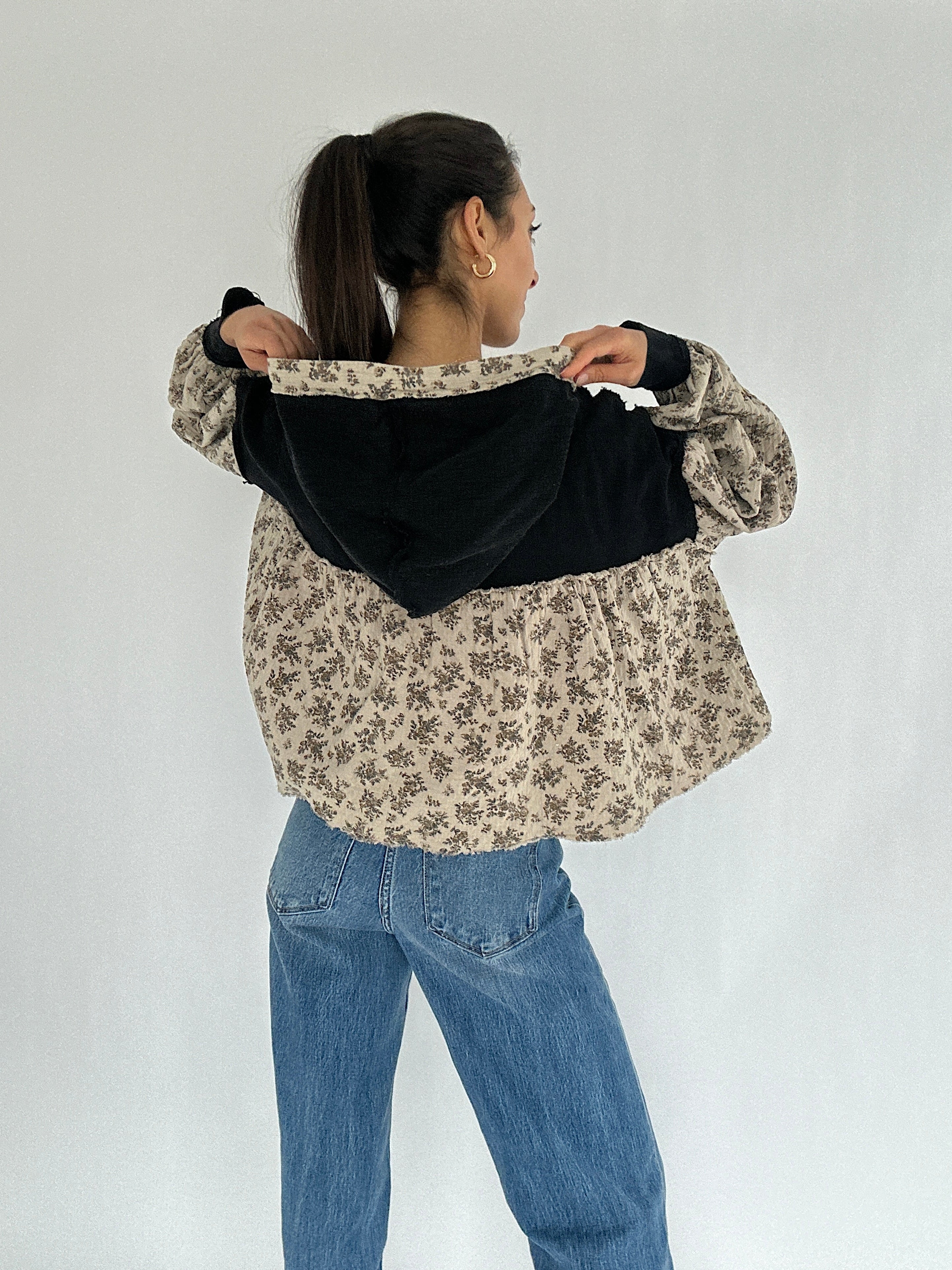 Person wearing a floral  and black hooded top with blue jeans on a white background