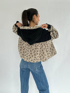 Person wearing a floral  and black hooded top with blue jeans on a white background