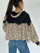 Person wearing a black and beige floral-patterned hoodie top with blue jeans on a white background showing the back