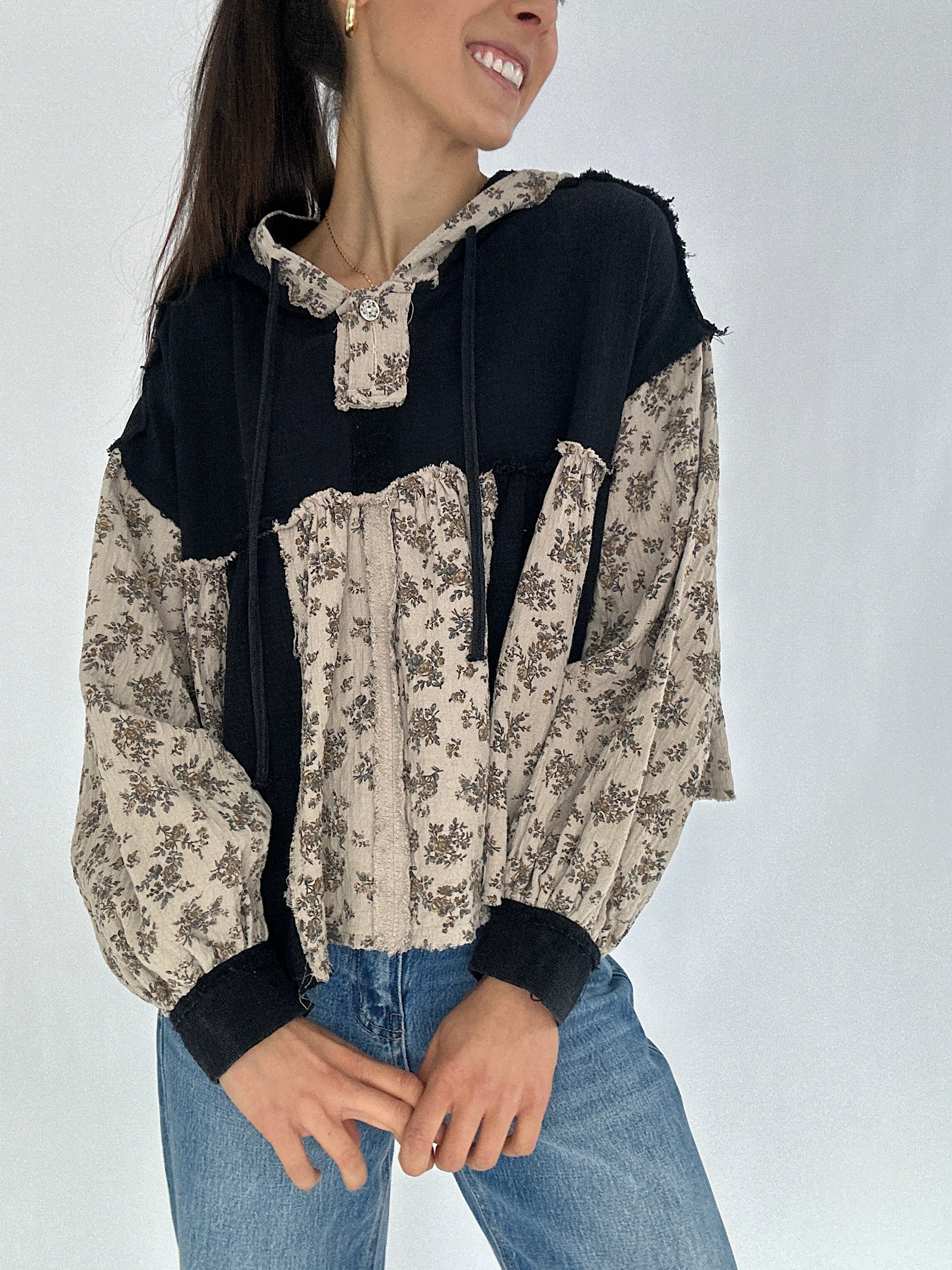 Woman wearing a black and beige floral top with blue jeans on a white background