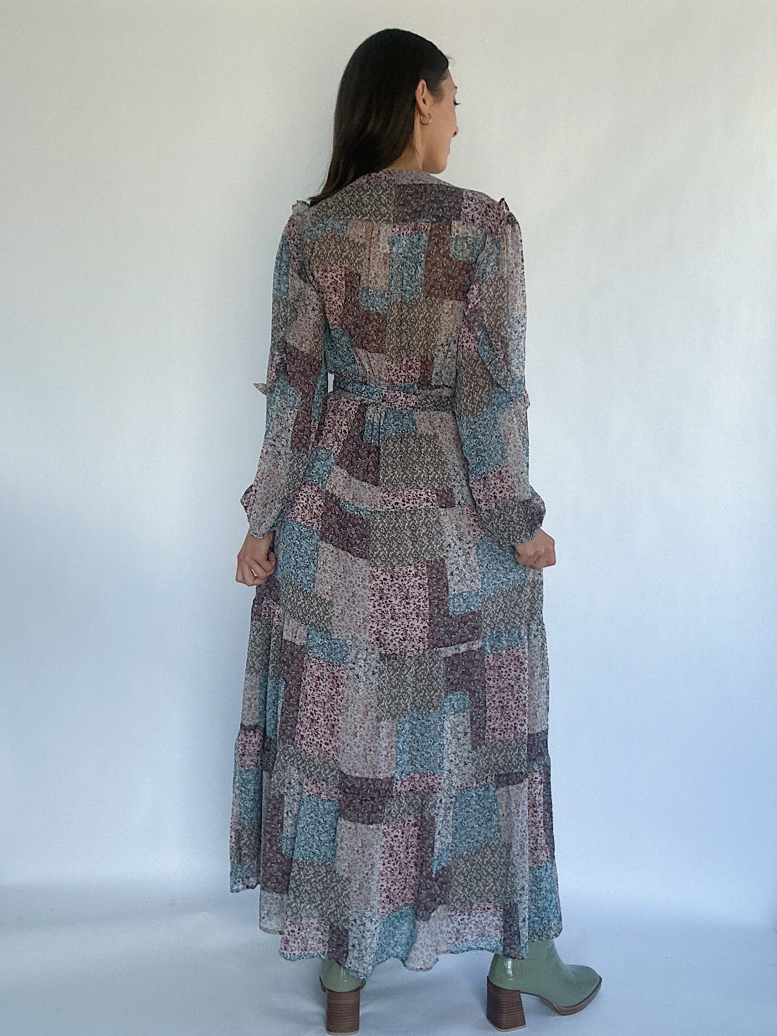 Woman wearing a long, patchwork patterned dress against a white background showing the back view