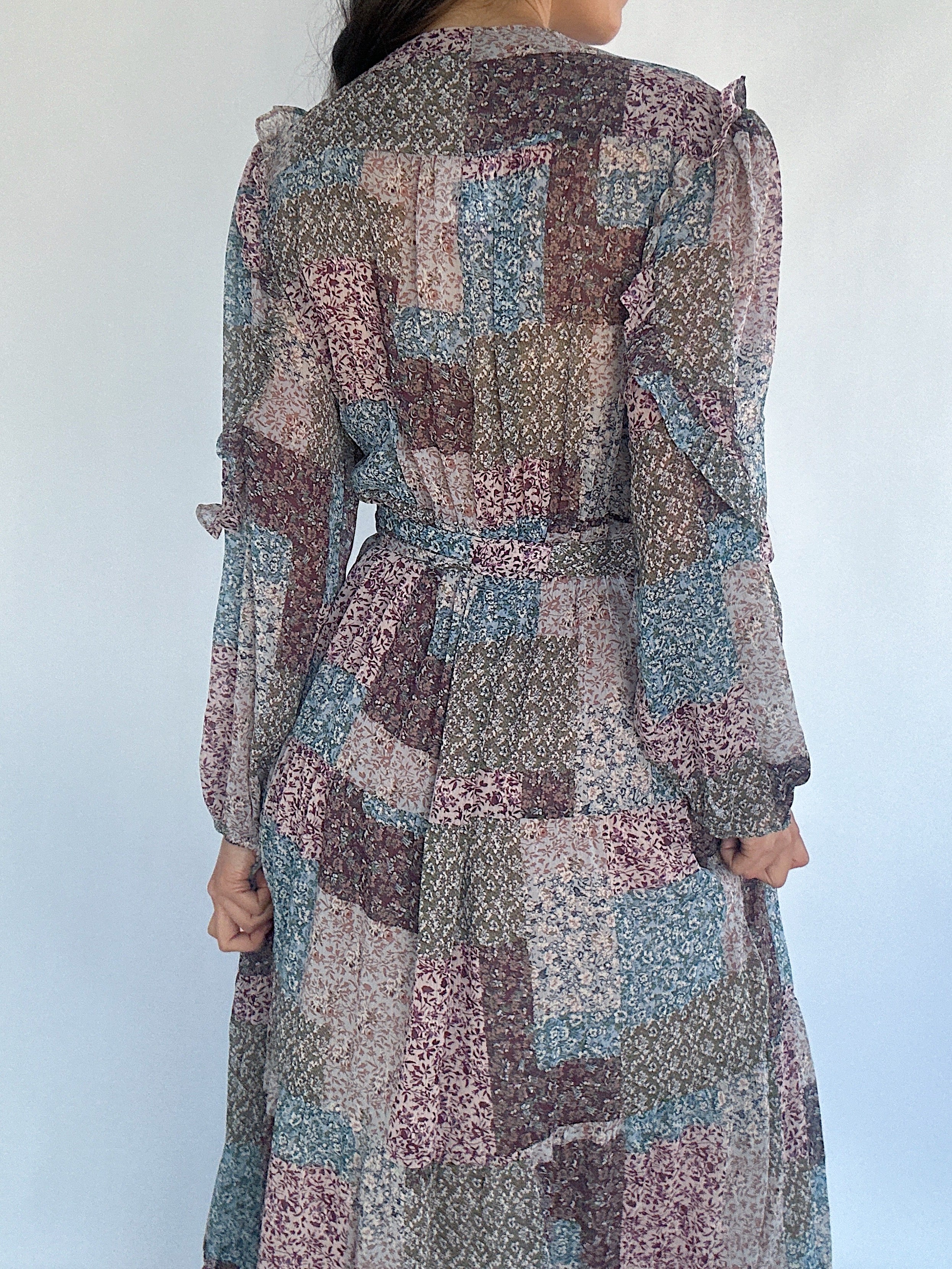 Long floral dress with a patchwork pattern worn by a person against a white background showing the back detail and waist tie