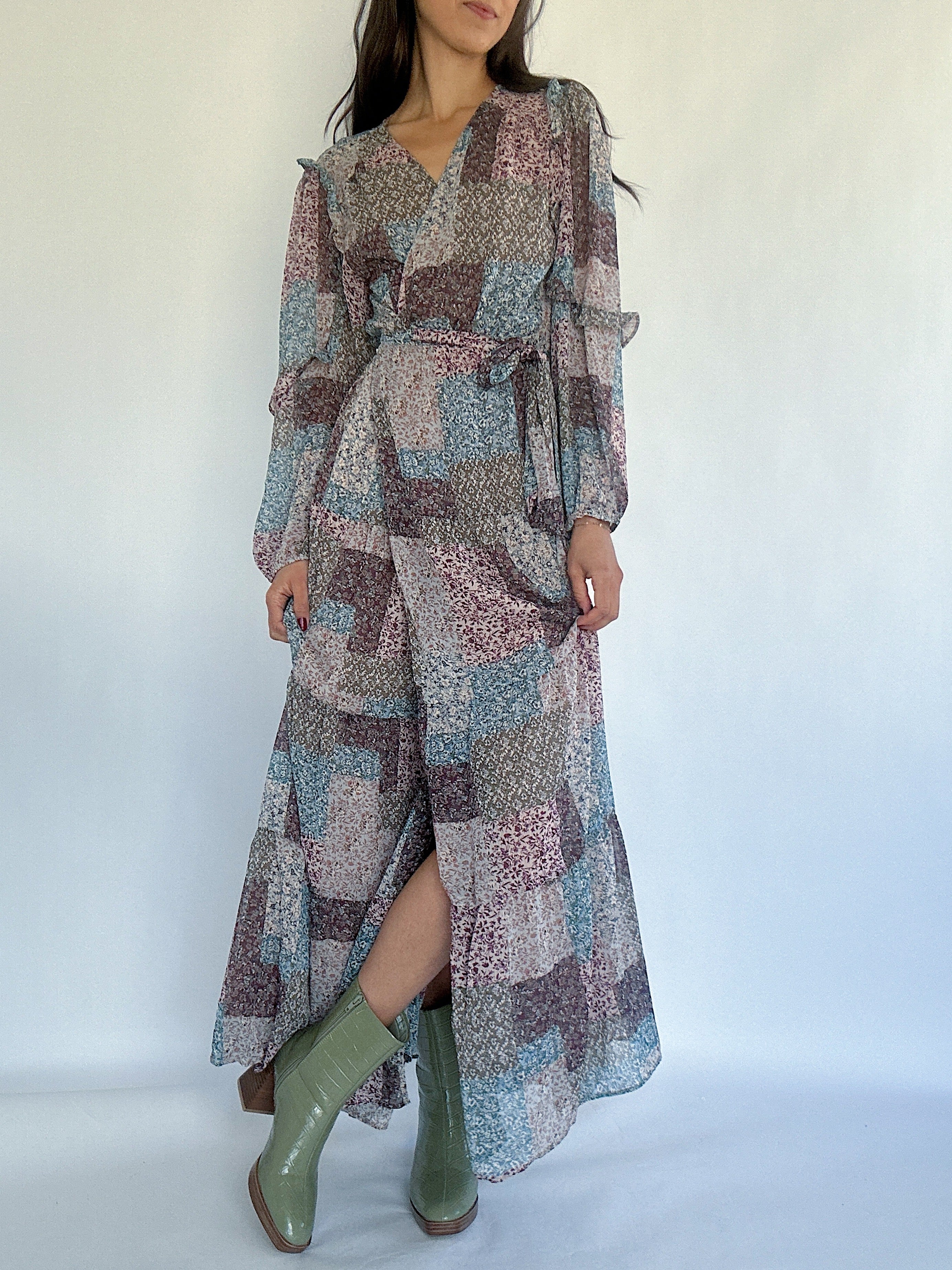 Woman wearing a long, patterned dress with green booties on a white background showing the slit in front