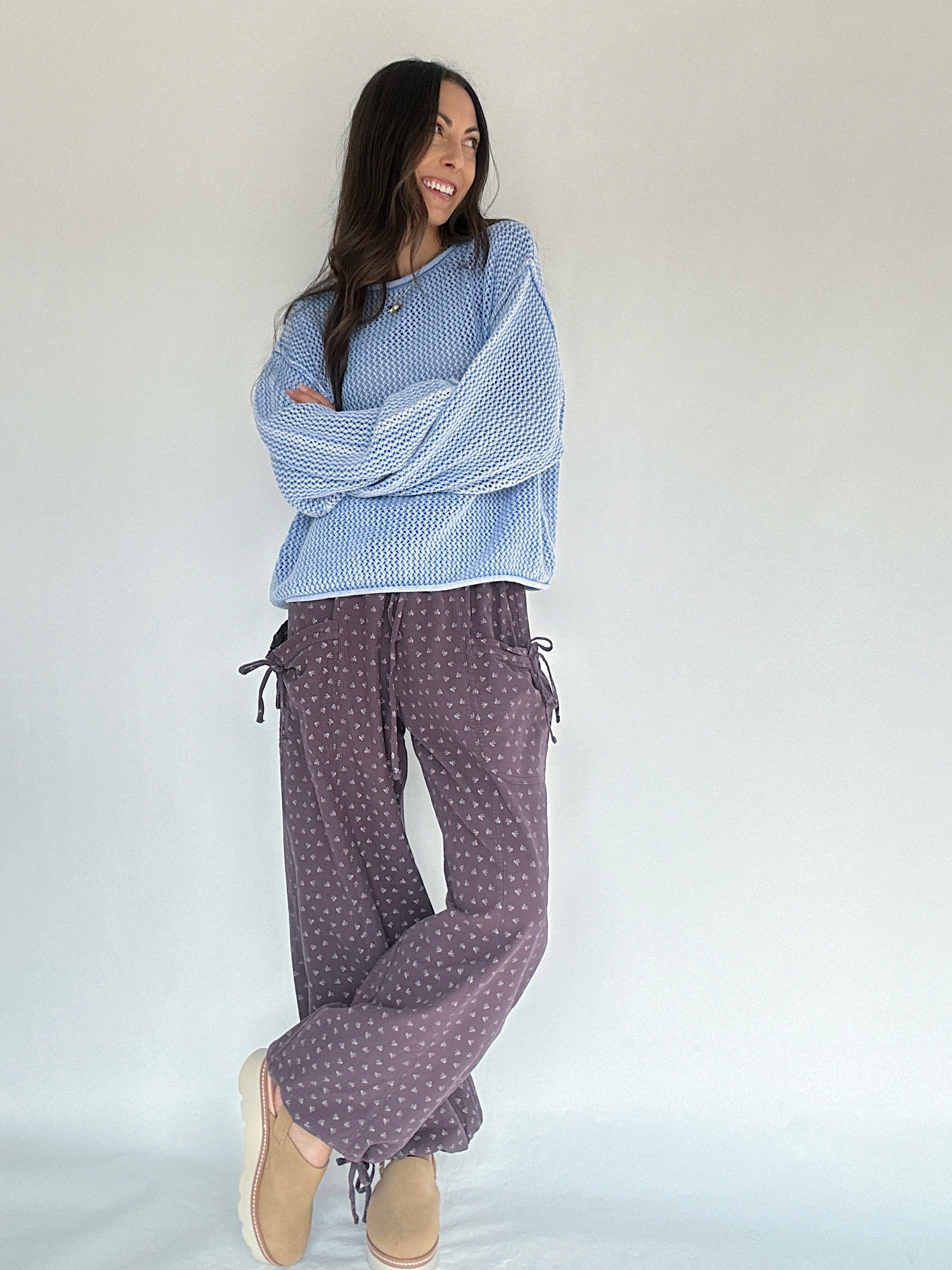 Woman wearing a blue patterned top and purple polka dot pants on a plain background