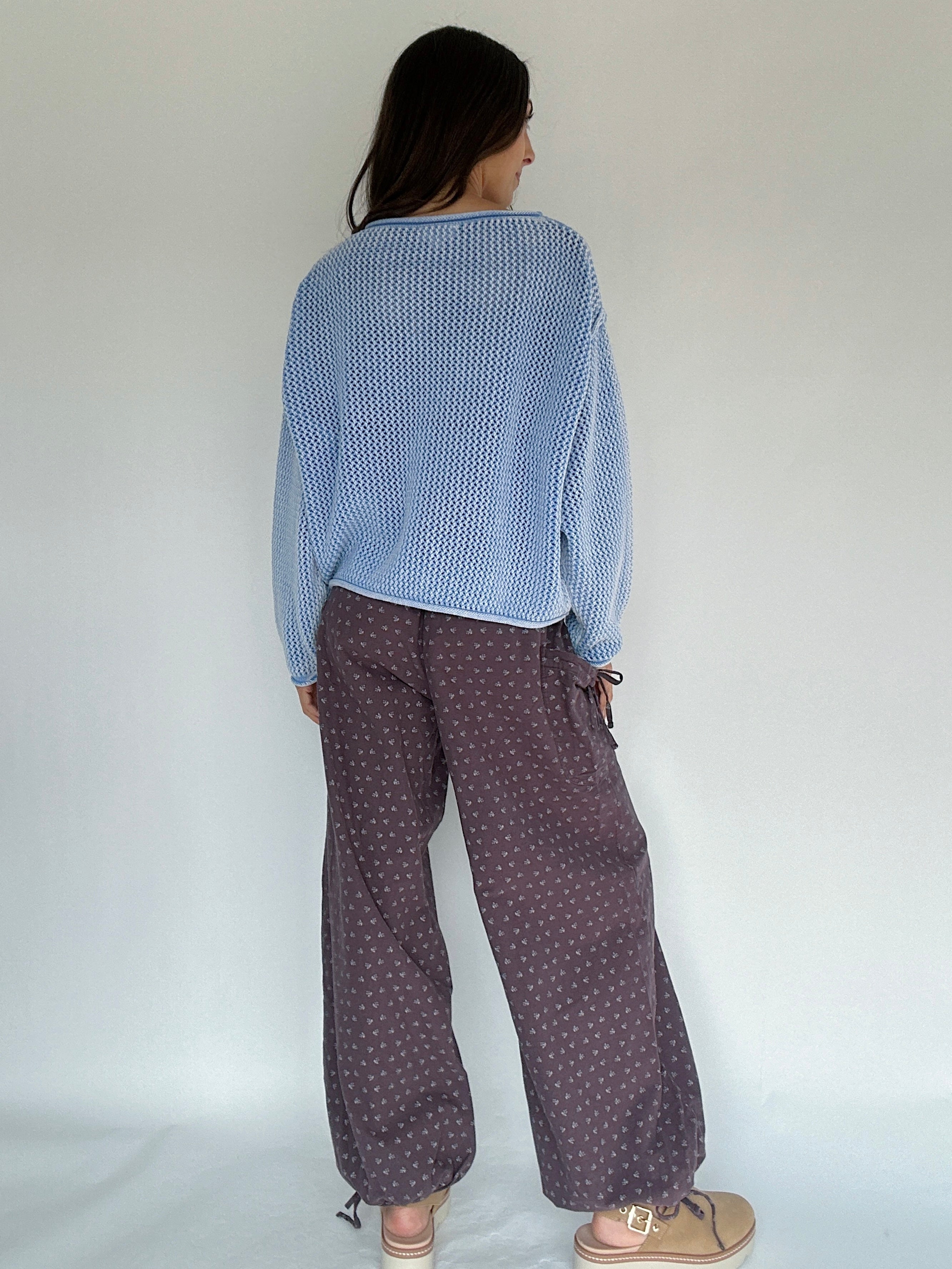 Person's back wearing a blue textured sweater and patterned brown pants against a white background 
