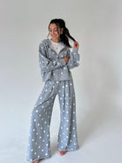 A woman modeling a matching gray and white polka dot loungewear set, consisting of a zip-up hoodie and wide-leg pants, against a plain light gray studio background.