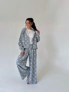 A woman modeling a gray two-piece loungewear set with white polka dots, consisting of a cropped zip-up hoodie and matching wide-leg pants, styled over a white t-shirt in a studio setting.