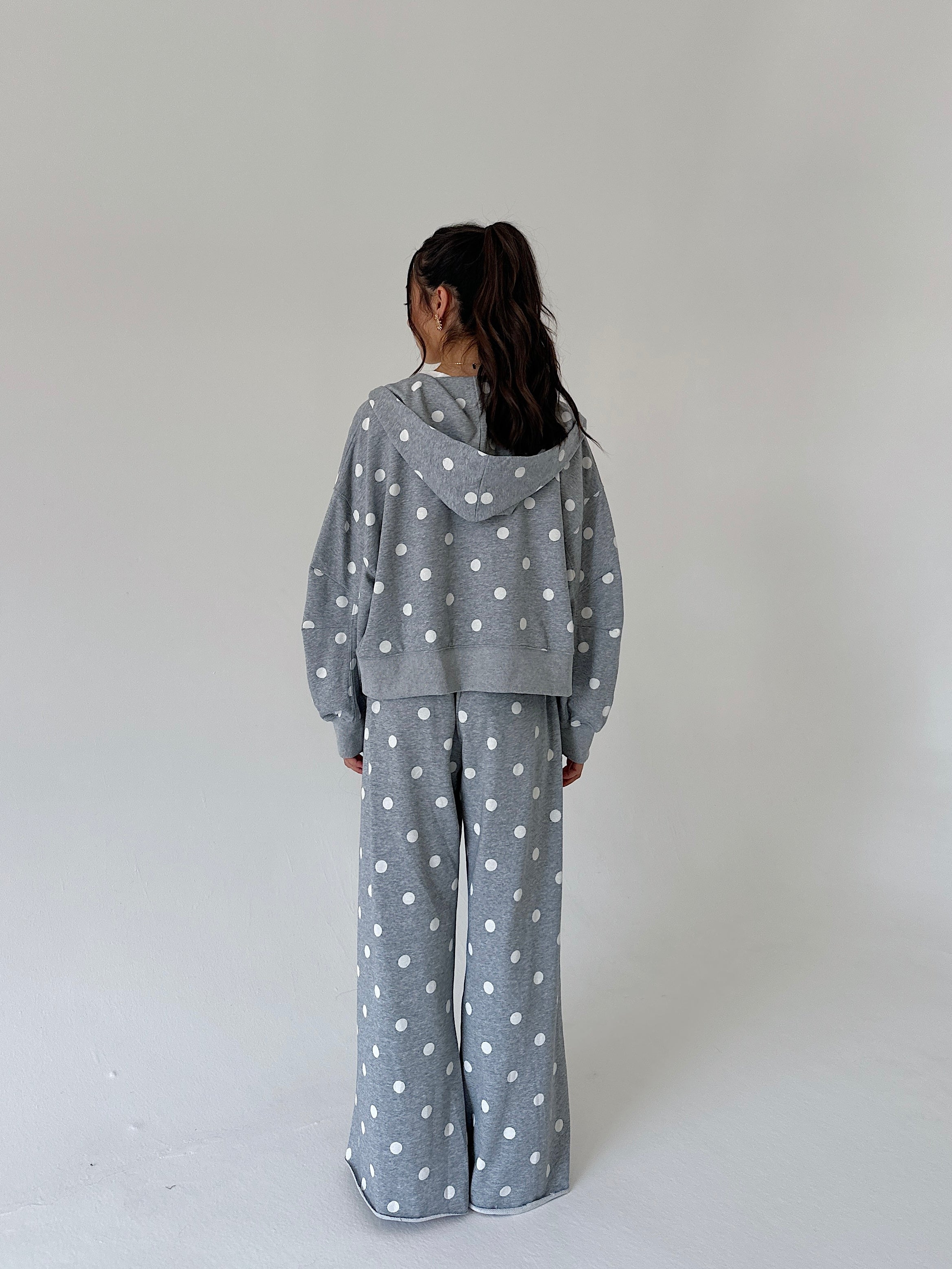 A model viewed from behind wearing a matching gray hooded sweatshirt and wide-leg pants set with a white polka dot pattern, set against a plain light gray studio background.