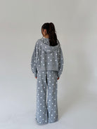 A model viewed from behind wearing a matching gray hooded sweatshirt and wide-leg pants set with a white polka dot pattern, set against a plain light gray studio background.