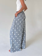 A person wearing wide-leg gray pants with a white polka dot pattern, paired with a white sleeveless top, standing against a plain light gray studio background.