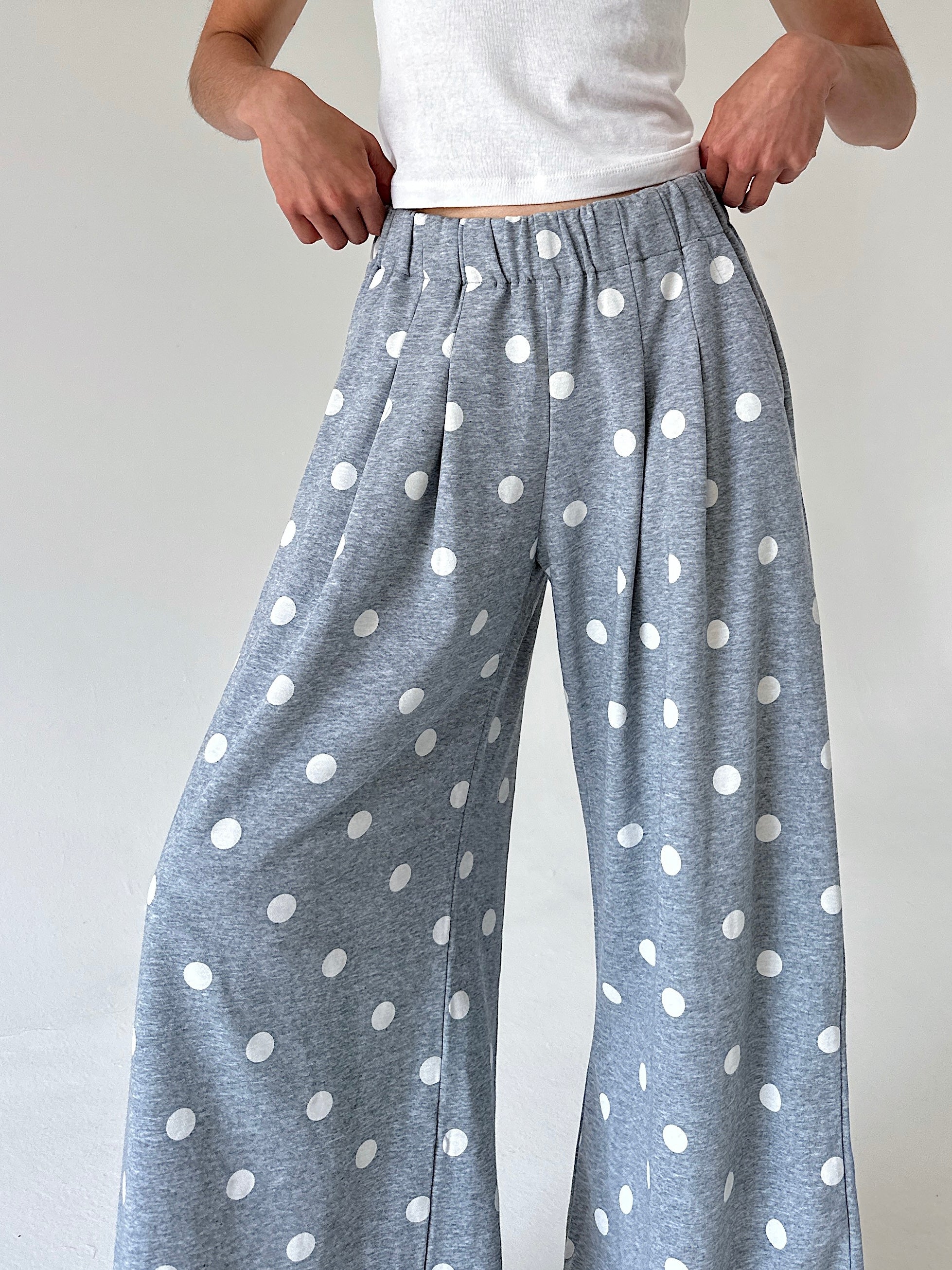 A person wearing loose, wide-leg lounge pants in heather gray with a white polka dot pattern, paired with a white tank top, shown from the waist down against a plain light background.