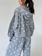 A woman wearing a heather gray hooded sweatshirt and matching sweatpants with a white polka dot pattern, shown from a side-back angle against a plain light gray wall.