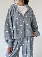 A person wearing a gray zip-up hoodie and matching sweatpants with white polka dots, styled over a white crewneck shirt against a plain light background.