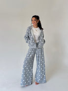 A woman modeling a matching gray two-piece loungewear set with white polka dots, consisting of a zip-up hoodie and wide-leg pants, styled over a white t-shirt against a plain light gray studio background.
