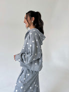 A woman wearing a gray hooded sweatshirt and matching sweatpants with white polka dots, shown in profile against a plain light gray studio background.