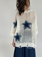 White knit sweater with blue star patterns worn by a person on a gray background showing back