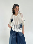 Woman wearing a white knit sweater with star patterns and blue jeans on a plain background