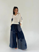Woman wearing a white and gray striped sweater with blue patchwork pants on a plain background