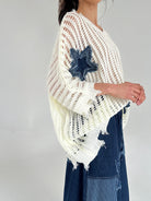 Person wearing a white knit top with denim accents on a plain background