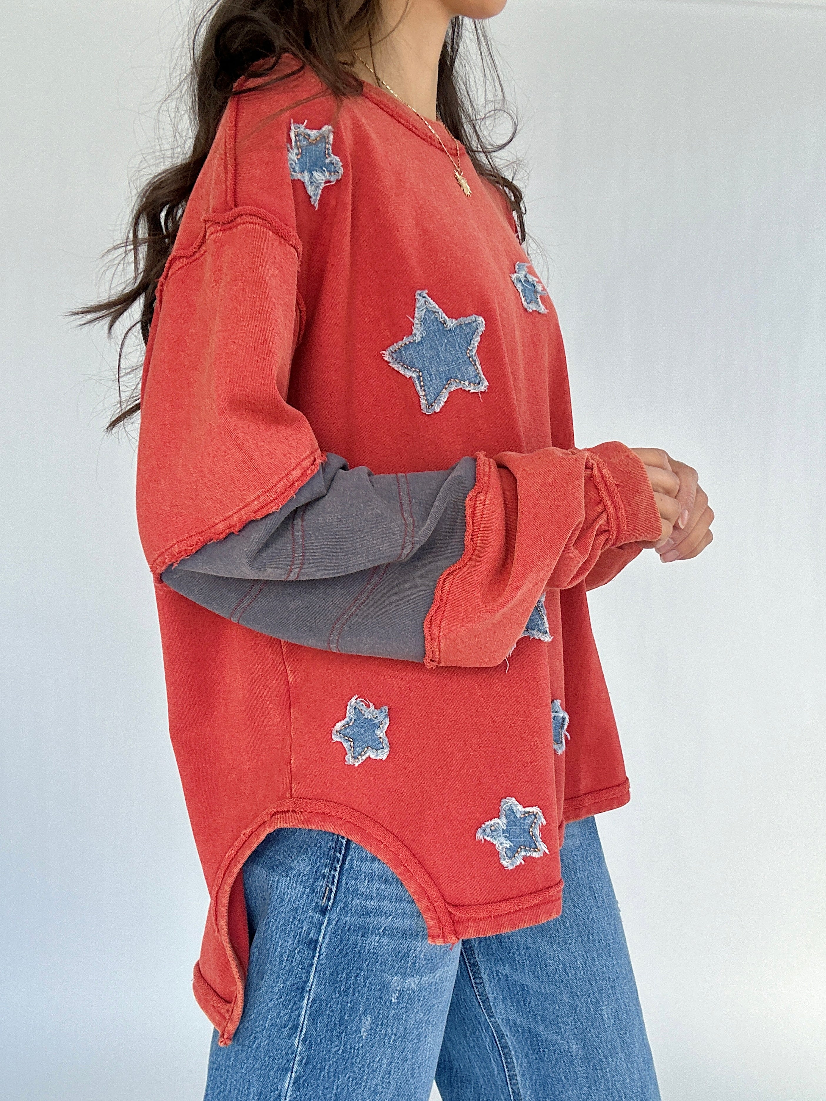 Person wearing a red long-sleeve shirt with blue star patterns and blue jeans on a white background