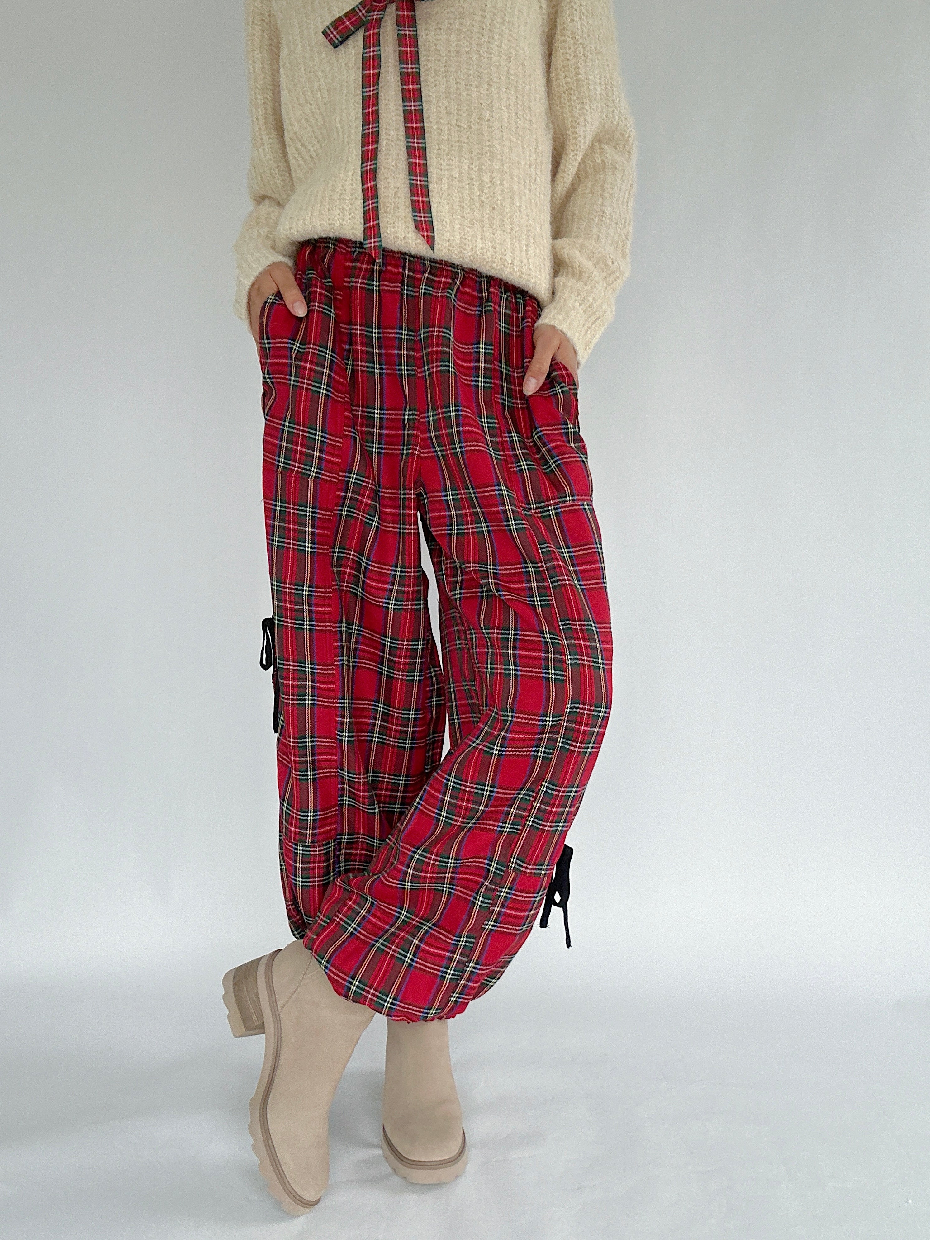 Person wearing red plaid pants with a cream sweater on a light gray background