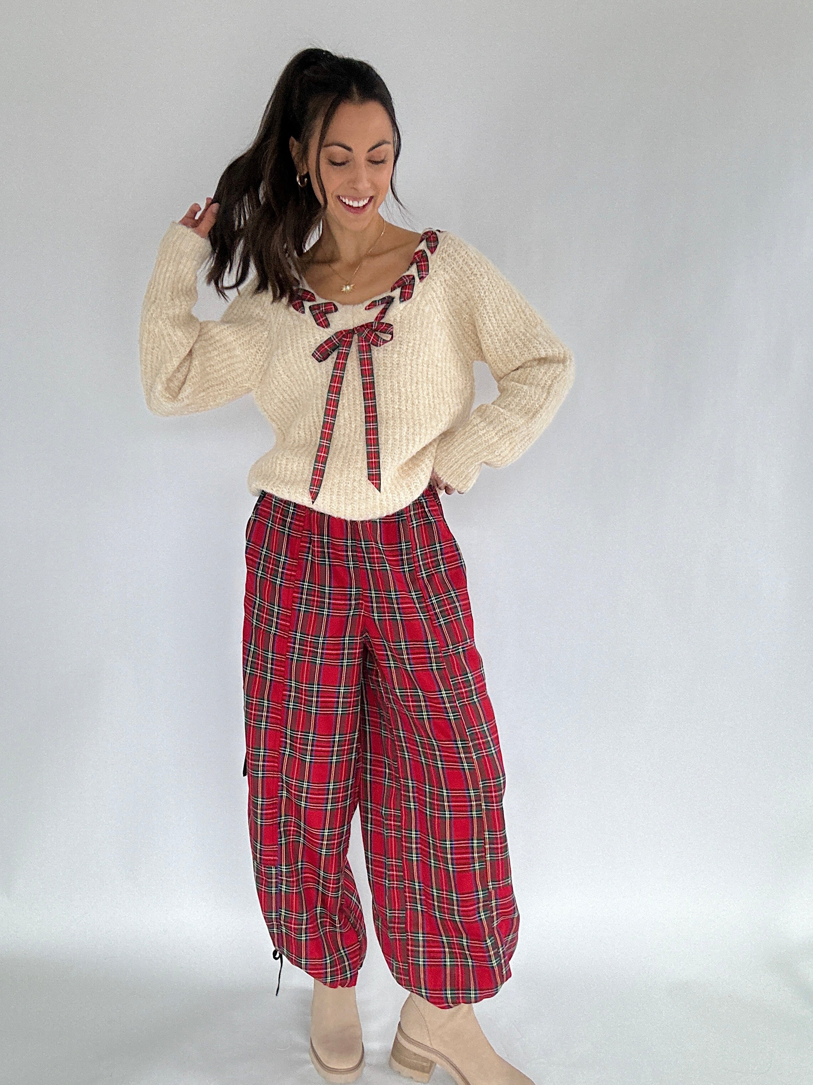 Woman wearing a cream sweater with a red plaid bow and red plaid pants on a white background