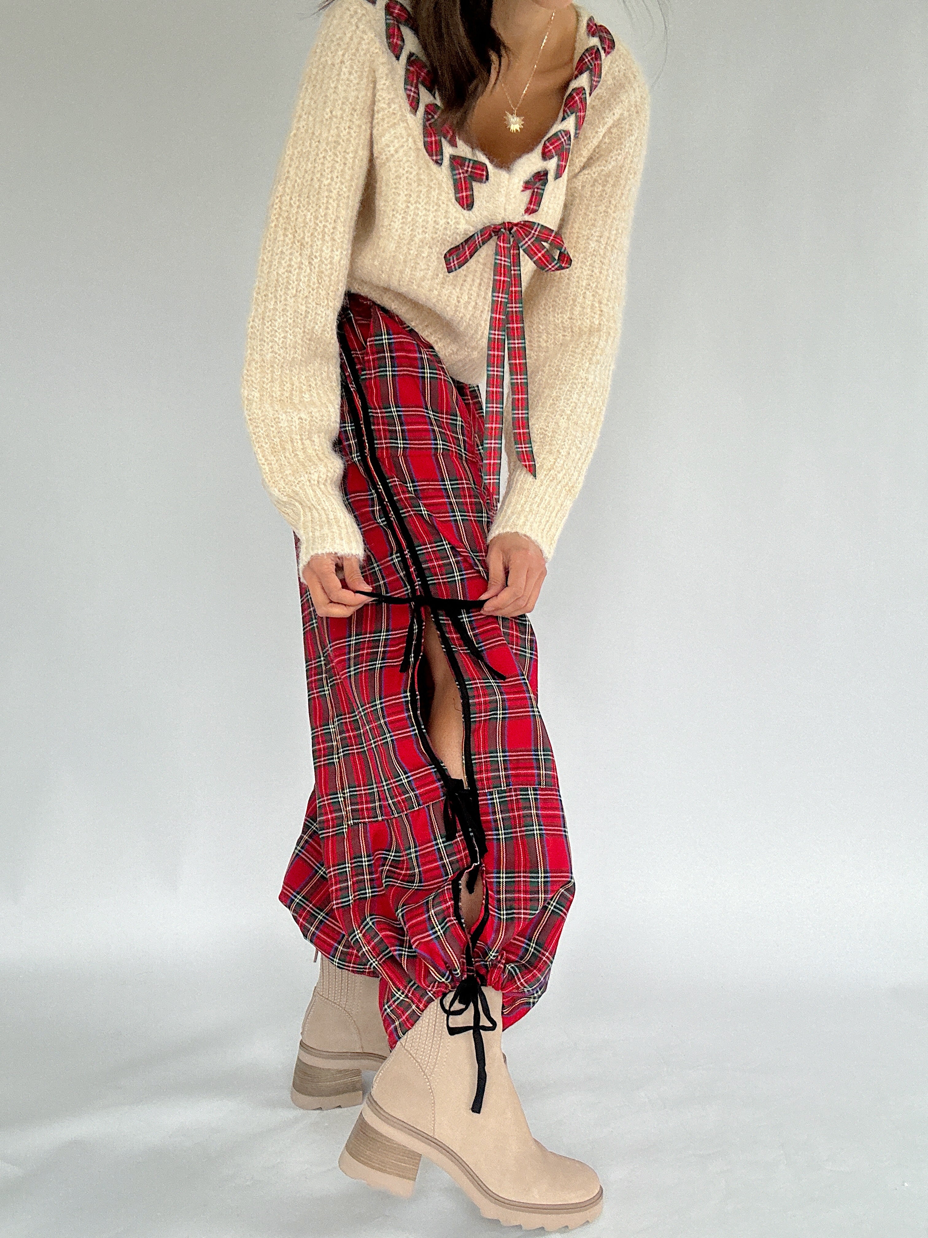 Person wearing a cream sweater with red plaid accents and a red plaid pants with ties on a white background