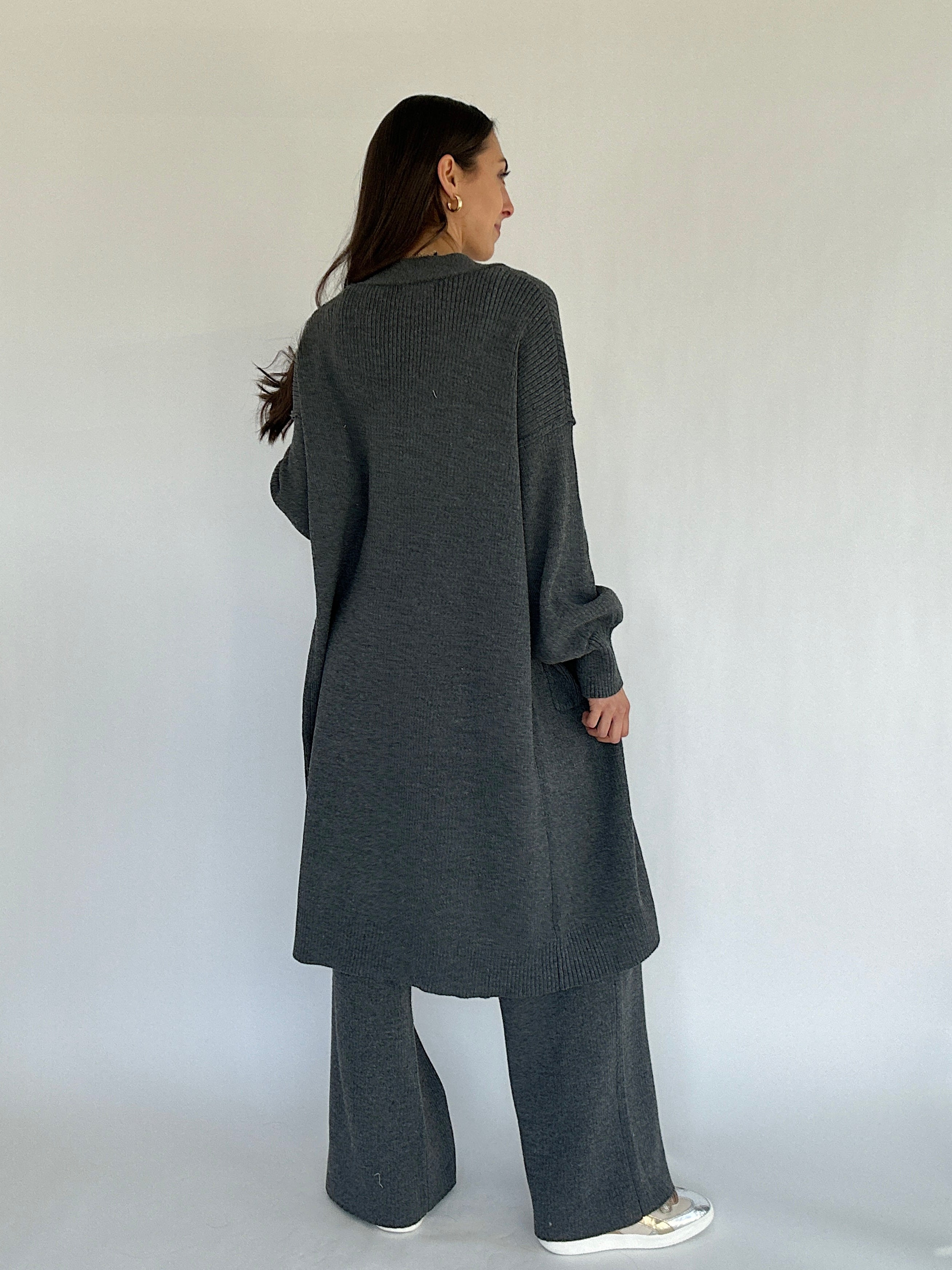 Person wearing a long dark gray cardigan and pants against a white background
