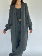 Person wearing a gray knit cardigan, top, and pants on a white background