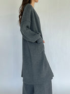 Person wearing a long gray cardigan and matching pants against a white background from side