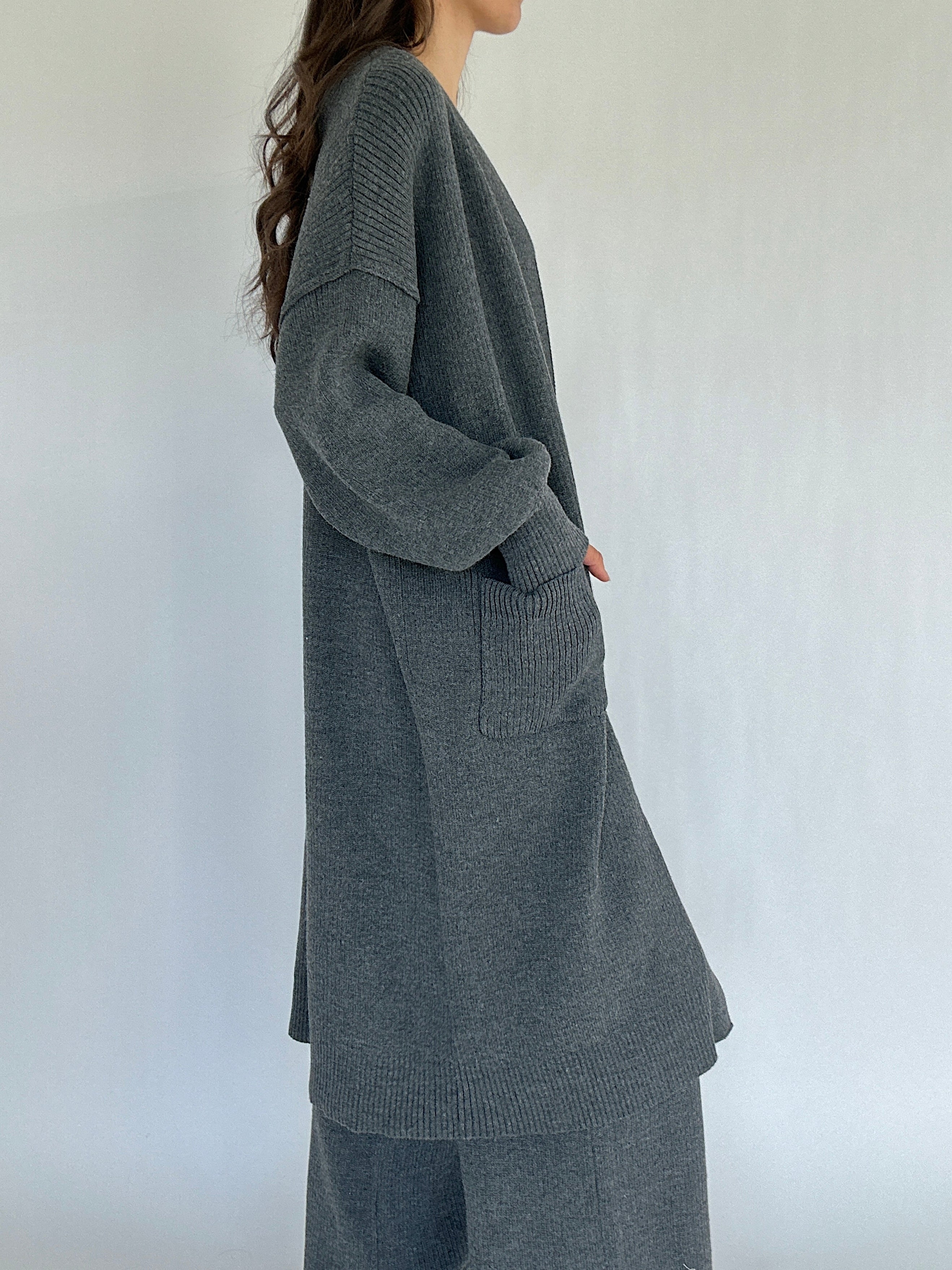 Person wearing a long gray cardigan and matching pants against a white background from side