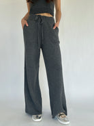 Person wearing dark gray knit pants with a tied waist on a plain background with hands in pockets