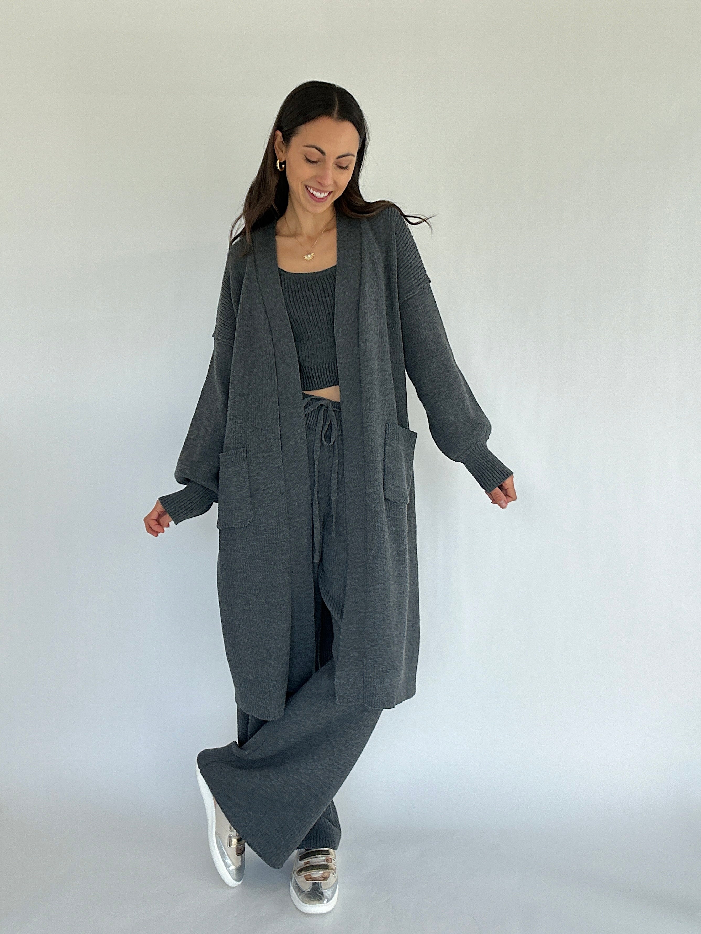 Woman wearing a matching gray long cardigan, top, and pants on a white background