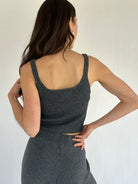 Woman wearing a gray ribbed tank top and pants against a plain background showing back