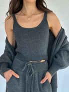 Person wearing a gray knit tank top with a matching cardigan against a white background