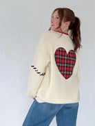Person wearing a cream sweater with a red plaid heart design on the back against a white background