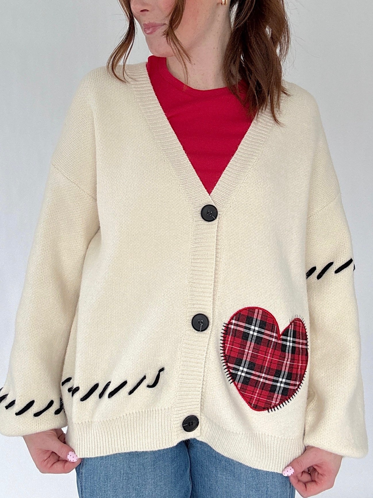 Person wearing a cream cardigan with a red plaid heart patch on a plain background