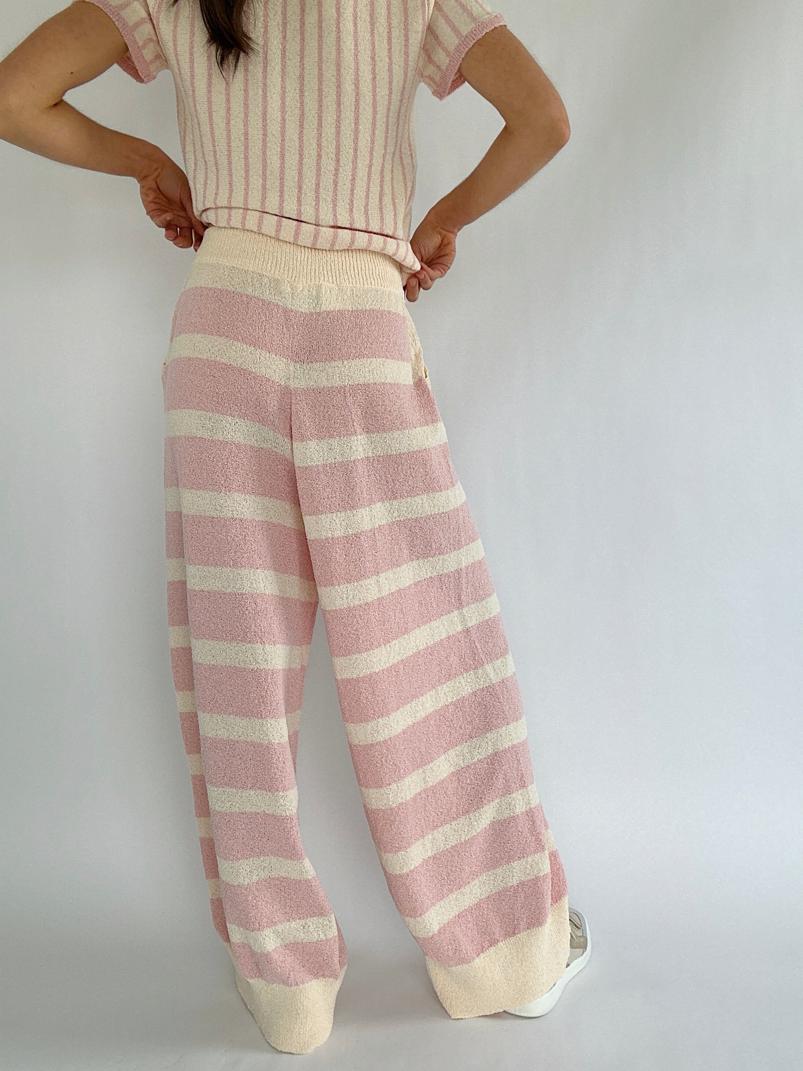 Person wearing a striped outfit with pink and cream pants on a plain background