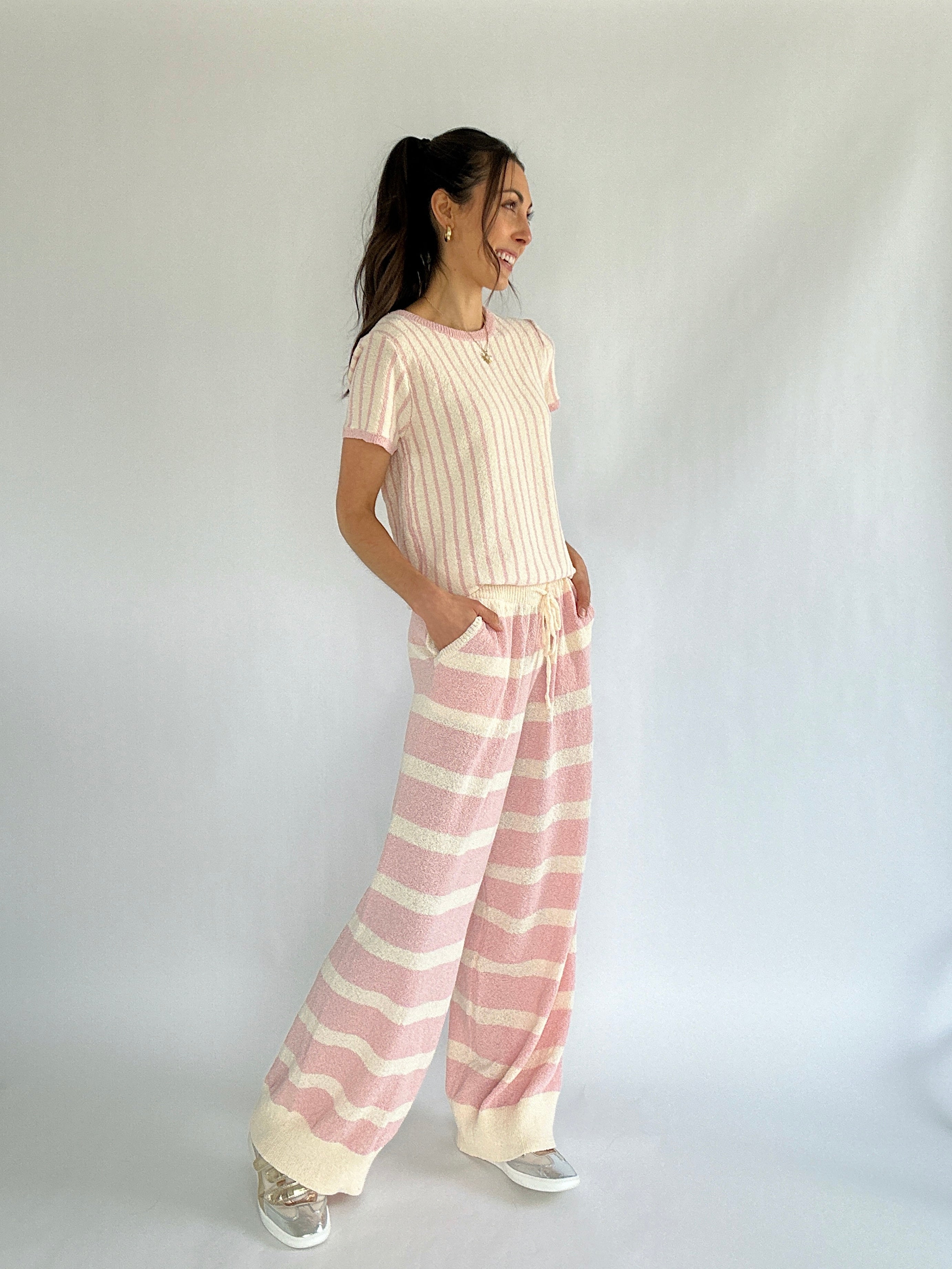 Woman wearing a cream top and pink striped pants against a white background