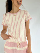 Woman wearing a pink and white striped knit short sleeve top and matching pants against a plain background