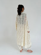 Person wearing a long, cream, knitted cardigan on a plain background showing back