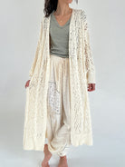 Person wearing a long cream knit cardigan over a green top and light pants on a white background
