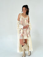 Woman wearing a floral dress with a lace cardigan and white boots on a white background