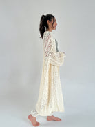 Woman wearing a long, light-colored knitted cardigan against a plain background from side